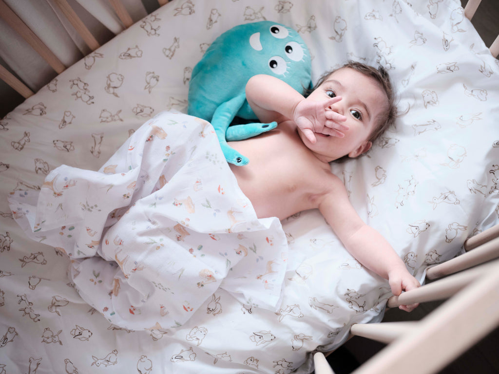 bébé coquin, allongé sur son lit à barreau avec un doudou et une main sur sa bouche